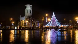 Pesepeda melintas depan pohon Natal raksasa yang berdiri di Alun-Alun Katedral di Vilnius, Lithuania, 1 Desember 2017. Konstruksi pohon ini menutupi area sekitar 2500 meter persegi dan diharapkan bisa menarik banyak pengunjung. (AP Photo/Mindaugas Kulbis)