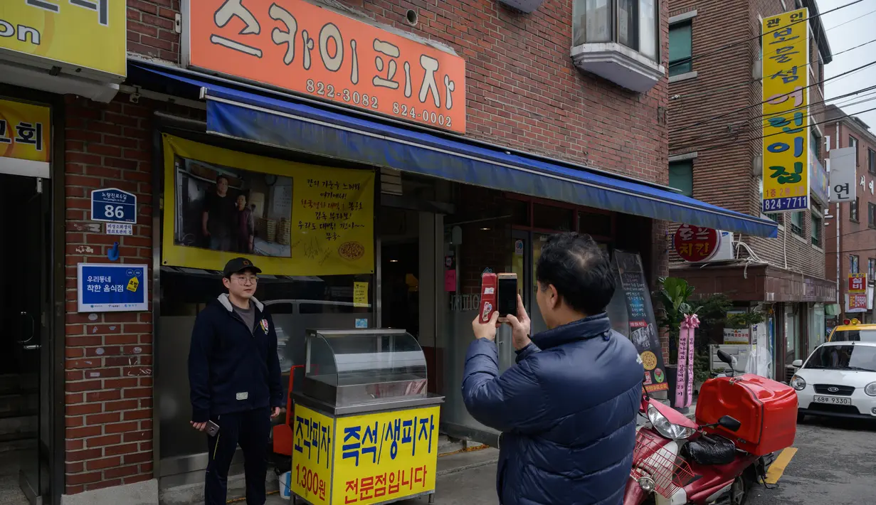 Seorang pria berpose di depan foto sutradara film Bong Joon-ho di restoran pizza bernama 'Sky Pizza' di Seoul, 13 Februari 2020. Lokasi syuting Parasite di Korea Selatan semakin ramai dikunjungi turis setelah film tersebut berhasil memboyong dan mendominasi di penghargaan Oscar 2020. (Ed JONES/AFP)