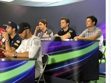 Rio Haryanto terlihat duduk santai diatas Lewis Hamilton dan Sebastian Vettel saat mengikuti sesi press conference jelang balapan Formula 1 2016 di Sirkuit Alber Park, Australia, Kamis (17/3/2016). (bola.com/Twitter/Manor Racing)