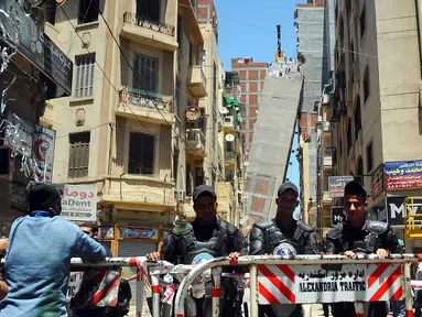 Aparat kepolisian menutup jalan dekat sebuah apartemen berlantai 13 yang mengalami kemiringan hingga mencapai blok apartemen lainnya di Alexandria, Mesir, Sabtu (3/6). Peristiwa itu memaksa polisi untuk mengevakuasi seluruh penghuni bangunan. (AP Photo)