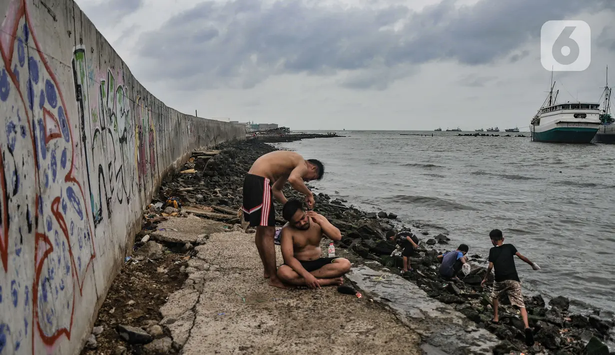 Warga mencukur rambut di pinggir laut kawasan Muara Baru, Jakarta, Rabu (19/1/2022). Badan Pusat Statistik (BPS) mencatat angka kemiskinan di Indonesia turun menjadi 26,5 juta orang per September 2021 dari sebelumnya mencapai 27,54 juta orang pada Maret 2021. (merdeka.com/Iqbal S Nugroho)