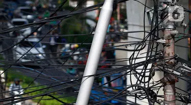 Kabel listrik dan kabel optik yang terlihat semrawut di kawasan Taman Puring, Jakarta, Jumat (3/7/2020). Kesemrawutan kabel ini sering terlihat di sejumlah kawasan Jakarta yang menyebabkan keindahan menjadi hilang dan pemandangan kurang enak untuk dilihat. (Liputan6.com/Johan Tallo)