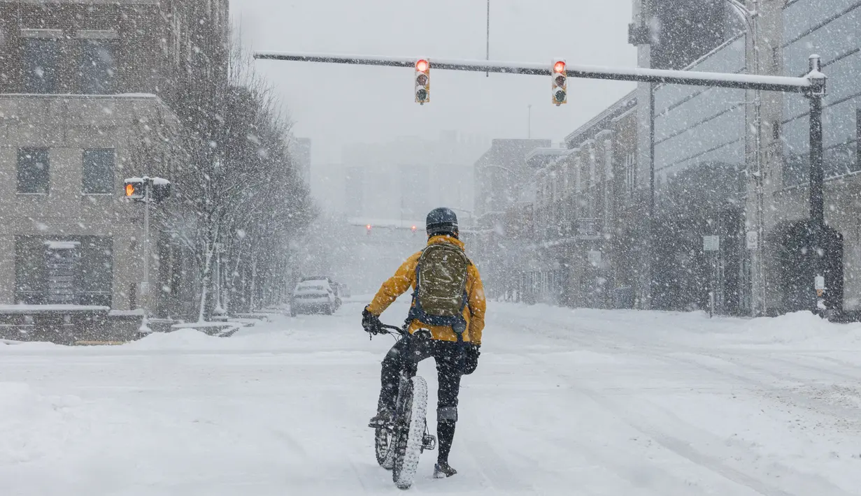 Seorang pria di sepedanya menunggu lampu merah selama badai salju di pusat kota Kalamazoo, Michigan, Rabu (2/2/2022). Badai musim dingin besar dengan jutaan orang Amerika di jalurnya membawa campuran hujan dan salju ke bagian tengah Amerika Serikat. (Joel Bissell/Kalamazoo Gazette via AP)