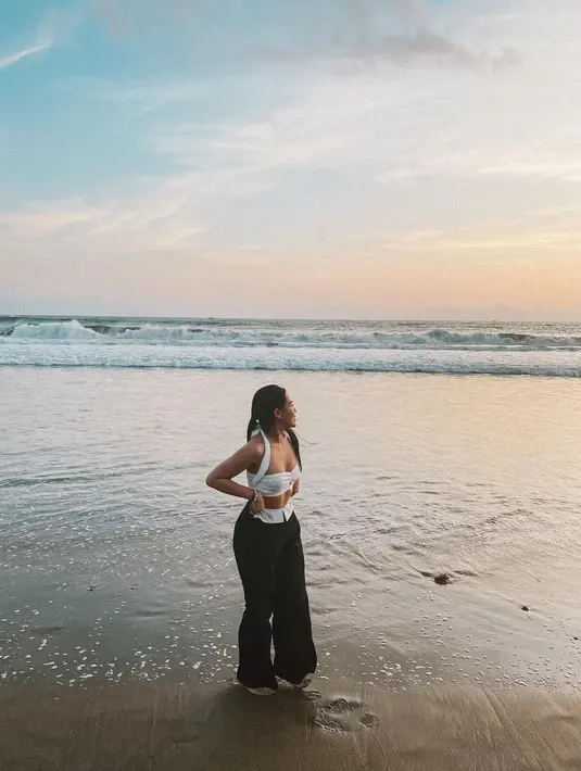 Melihat gaya chic Aaliyah Massaid main di pantai. Ia mengenakan atasan cropped bra putih dengan detail halter-neck, dipadu mengenakan celana panjang hitam. [Foto: Instagram/aaliyah.massaid]
