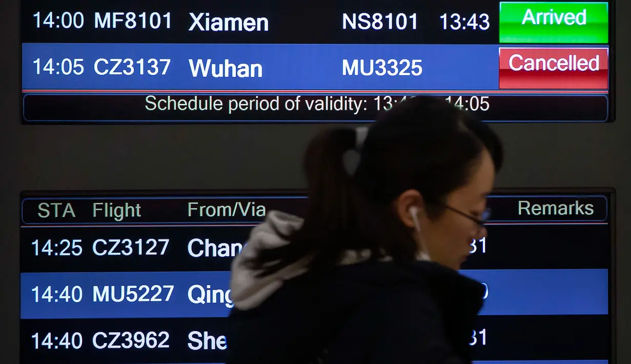 Seorang pelancong melewati papan informasi penerbangan dari Wuhan yang dibatalkan di Bandara Internasional Ibu kota Beijing, 23 Januari 2020. Pemerintah China memutuskan menutup seluruh akses masuk dan keluar Kota Wuhan untuk mencegah penyebaran wabah virus corona. (AP/ Mark Schiefelbein)