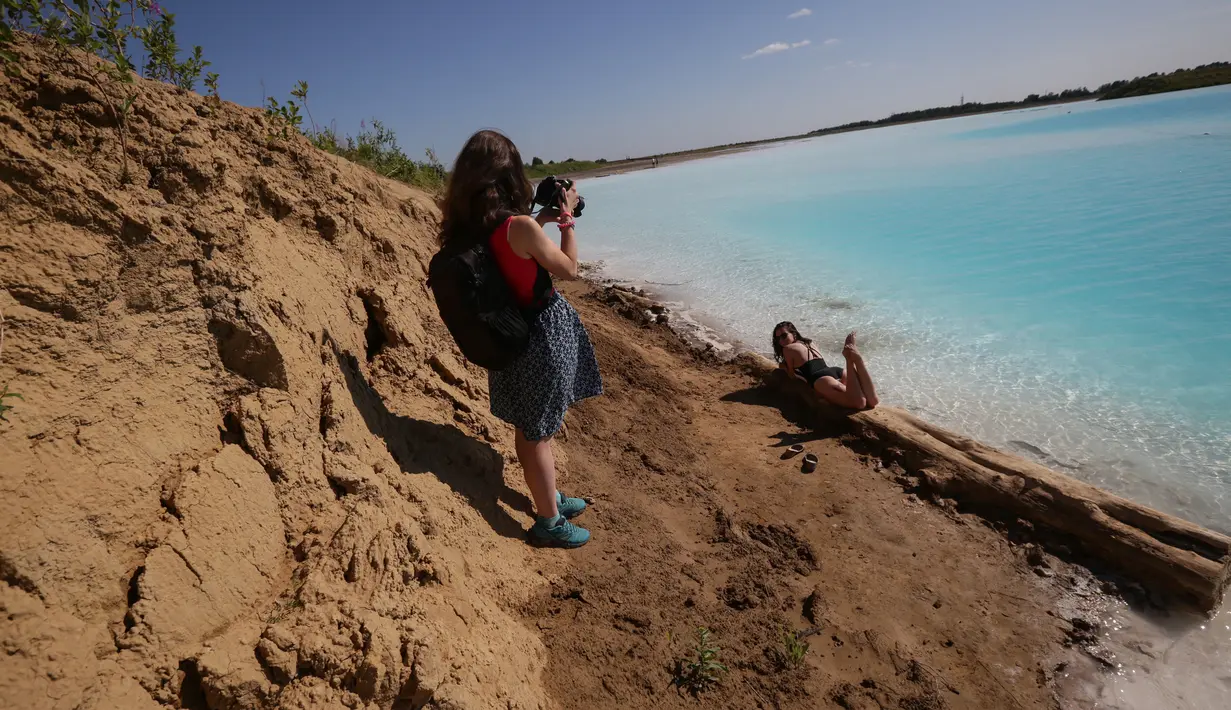 Pengunjung berpose saat mengunjungi tempat pembuangan abu dari pabrik batubara lokal yang sering disebut 'Maladewa di Siberia' di Danau Novosibirsk, Rusia, Kamis (11/7/2019). Warna biru terang danau itu berasal dari garam kalsium dan oksida logam yang tercampur di dalamnya. (Rostislav NETISOV/AFP)