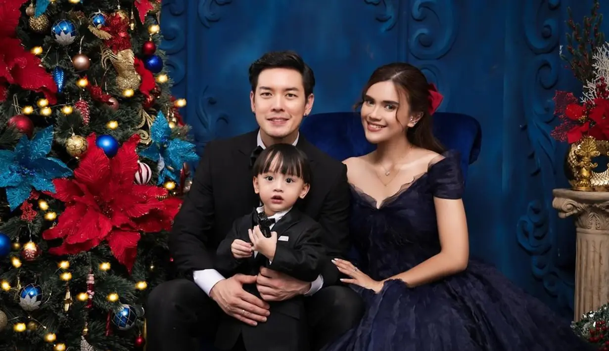 Background warna biru dongker selaras dengan gaun Audi Marissa dan beberapa pernak Pernik pohon Natal. Audi tampil memesona off shoulder dan gaya rambut ikat setengah. Pita warna merah di rambutnya juga mendukung penampilan Audi jalani pemotretan tema Natal. Anthony Xie gagah dengan jas hitam dan dasi kupu-kupu, yang di mana busananya selaras dengan sang anak. (Liputan6.com/IG/@audimarissa)