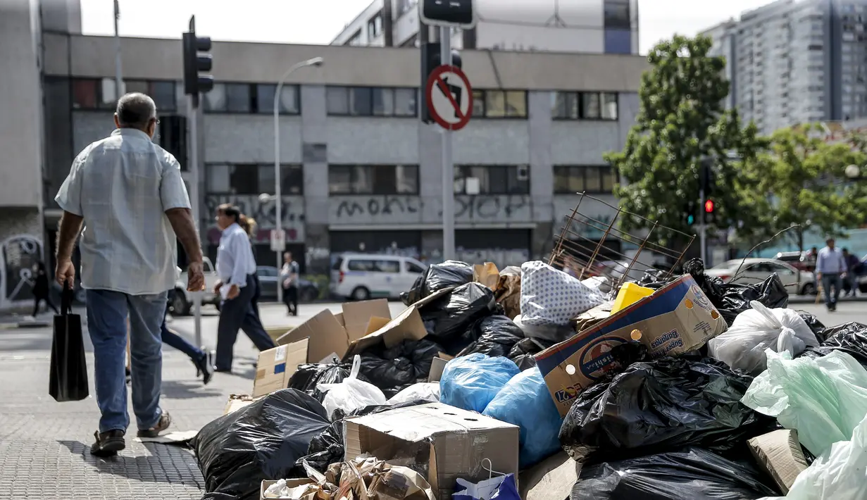 Orang-orang berjalan melewati tumpukan sampah yang diakibatkan pemogokan petugas sampah di Santiago (14/11/2019). Demo yang semakin keras juga disertai aksi mogok nasional termasuk petugas sampah di negara kaya minyak di Amerika Selatan tersebut.  (AFP/Javier Torres)