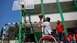 Seorang pria yang menggunakan kursi roda melempar bola ke dalam ring saat bermain basket di lapangan sekolah milik pemerintah di Kota Gaza (4/4). (AP Photo/Hatem Moussa)