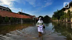 Siswi berjalan melewati banjir yang menggenangi halaman  sekolah di SMAN 4 Tangsel, Pondok Ranji, Tangerang Selatan, Banten, Selasa (14/6/2022). Tiga  pekan lebih banjir merendam lapangan sekolah itu dikarenakan tertutupnya saluran air oleh sampah yang berasal dari tempat pembuangan sampah (TPS) ilegal. (merdeka.com/Arie Basuki)