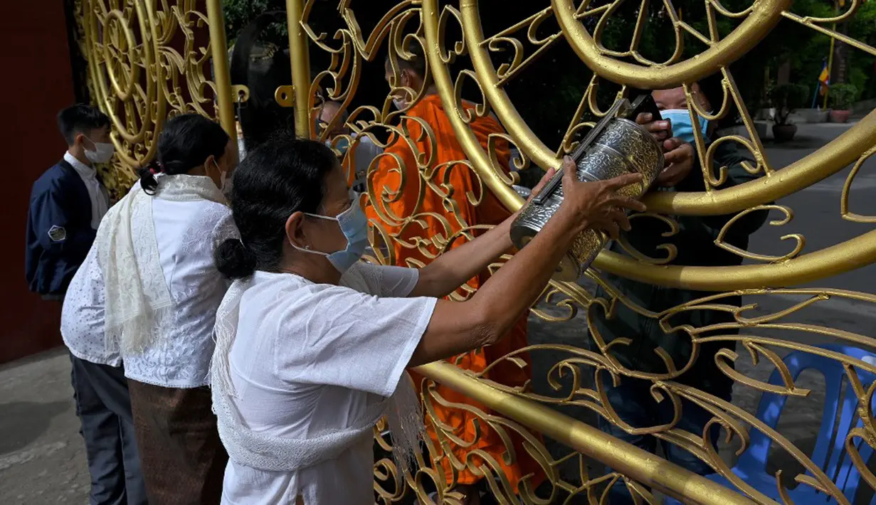 Warga memberikan makanan dan sedekah kepada biksu Buddha saat Festival Pchum Ben (Festival Kematian) di luar pagoda di Phnom Penh, Kamboja, 24 September 2021. Pihak berwenang menghentikan perayaan Festival Kematian karena pandemi COVID-19. (TANG CHHIN Sothy/AFP)