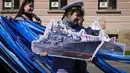 Wanita membawa gambar kapal perang berbaris dengan latar belakang lembaran yang yang dipajang di jendela menggambarkan huruf Z simbol militer Rusia selama perayaan memperingati 318 tahun kota Kronstadt di luar St. Petersburg, Rusia (21/5/2022). (AP Photo/Dmitri Lovetsky)