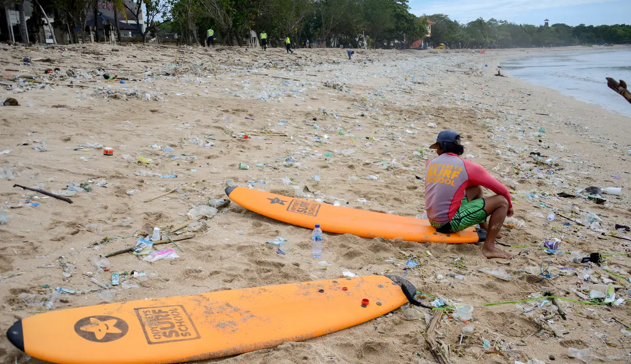 Peselancar duduk di antara sampah kiriman yang terdampar di pesisir pantai Kuta, Bali, Kamis (31/12/2020). Pantai Kuta tampak sepi menyusul aturan larangan pesta perayaan pergantian tahun baru dan pemberlakuan jam malam untuk pengendalian aktivitas masyarakat yang dibatasi. (SONNY TUMBELAKA / AFP)