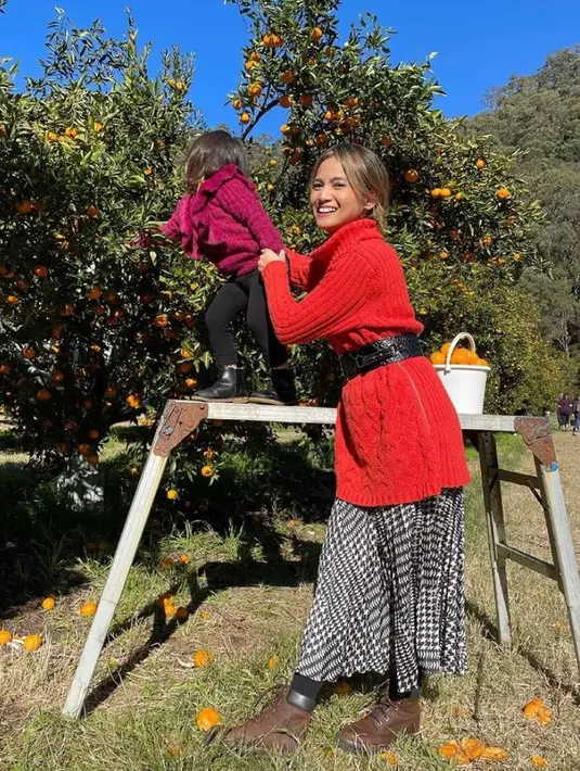 Liburan ke kebun jeruk, Acha tampil modis mengenakan knit sweater warna merah dengan pleats skirt dan aksesori belt. Senada dengan sang ibunda, Bridgia tampak mengenakan knit sweater serupa warna merah dan legging hitam. (Instagram/septriasaacha).