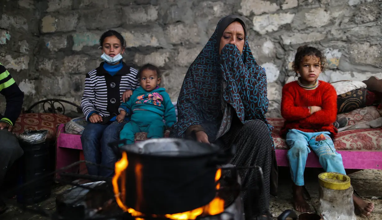 Warga Palestina menghangatkan diri di sekitar api tungku di area permukiman kumuh sebuah kamp pengungsi saat cuaca badai di Kota Khan Younis, Jalur Gaza selatan, pada 26 November 2020. (Xinhua/Yasser Qudih)