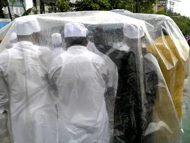 Umat ​​muslim berlindung di bawah lembaran plastik saat melaksanakan sholat Idul Adha pada pagi hari yang diguyur hujan di Mumbai, India, Kamis (29/6/2023). (Photo by INDRANIL MUKHERJEE / AFP)