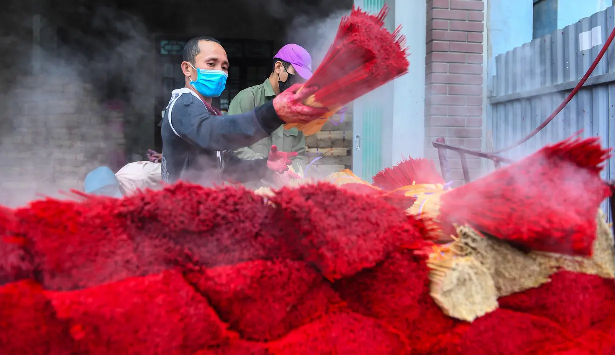 Seorang pekerja mewarnai dupa di sebuah bengkel di desa Quang Phu Cau di pinggiran Hanoi, Vietnam, Rabu (12/1/2022). Penduduk desa sibuk menyiapkan ratusan ribu dupa untuk menyambut perayaan Tahun Baru Tet, Imlek versi Vietnam di Februari nanti. (Nhac NGUYEN/AFP)