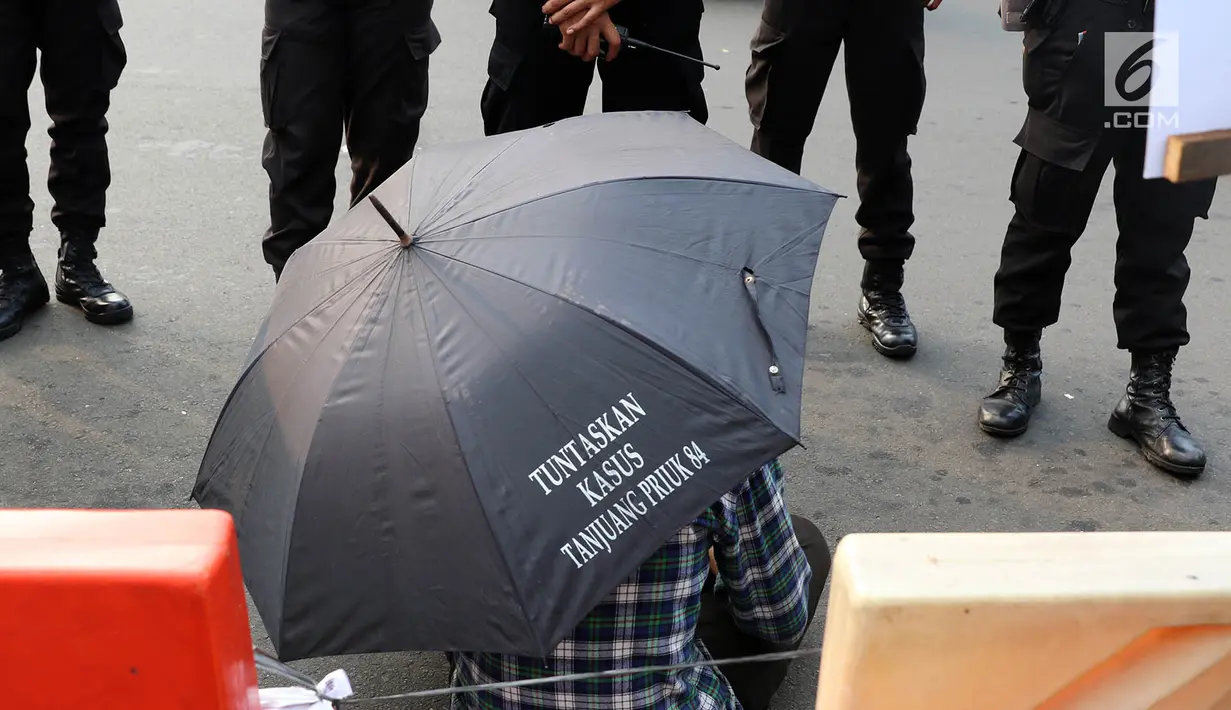 Seorang peserta aksi membawa payung hitam yang bertuliskan "Tuntaskan Kasus Tanjuang Priuk 84" saat menggelar aksi kamisan ke-493 di depan Istana Negara, Jakarta, Kamis (18/5). (Liputan6.com/Immanuel Antonius)