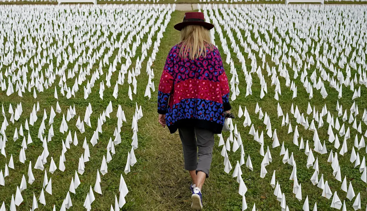 Seniman Suzanne Brennan Firstenberg berjalan di antara ribuan bendera putih yang ditanam untuk mengenang warga Amerika yang meninggal karena COVID-19 di dekat Stadion RFK di Washington, Selasa (27/10/2020). Instalasi seni publik ini disebut "In America, How Could This Happen.” (AP/Patrick Semansky)