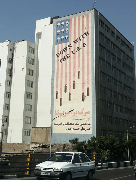 Kendaraan melintasi mural yang menggambarkan bendera Amerika Serikat (AS) di sepanjang dinding bekas Kedutaan AS di Ibu Kota Teheran, Iran, Sabtu (22/6/2019). (ATTA KENARE/AFP)