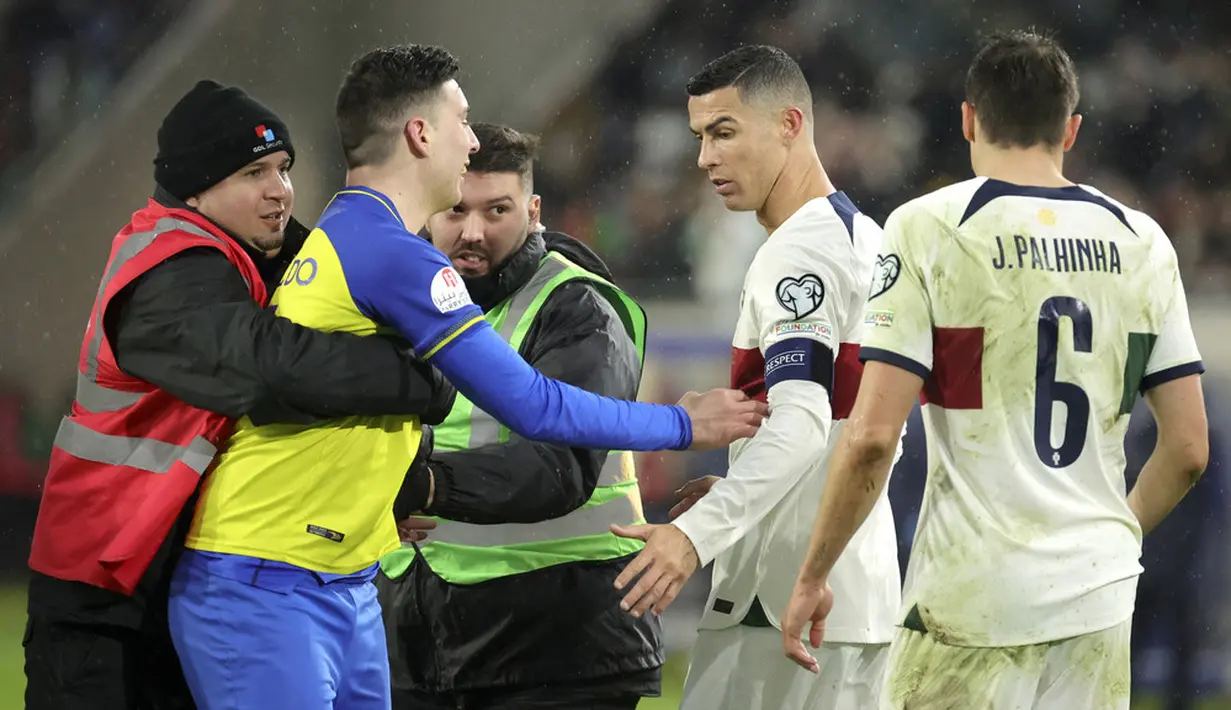 Petugas mengamankan seorang suporter yang berusaha mendekati pemain Portugal, Cristiano Ronaldo saat pertandingan melawan Luksemburg pada matchday kedua Grup J Kualifikasi Euro 2024 di Stadion Stade de Luxembourg, Senin (27/3/2023). (AP Photo/Olivier Matthys)