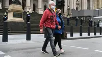 Orang-orang menyeberang jalan sementara polisi berjaga di tangga parlemen negara bagian Victoria di Melbourne, Australia, Kamis (30/9/2021). Melbourne bergulat dengan lonjakan infeksi Covid-19 di mana sebanyak 1.438 kasus dilaporkan, jumlah harian terbesar sejak awal pandemi. (William WEST / AFP)