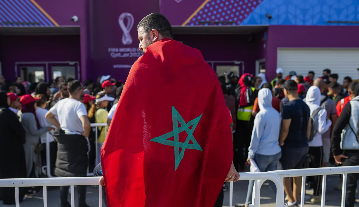 Seorang pria berbalut bendera Maroko mengantre dengan suporter di luar Stadion Al Janoub di Wakrah, dengan harapan mendapatkan tiket pertandingan sepak bola semifinal Piala Dunia 2022 antara Prancis vs Maroko, Selasa (13/12/2022). Partai hidup mati akan tersaji antara timnas Prancis melawan Maroko pada babak semifinal Piala Dunia 2022 di Stadion Al Bayt, Kamis (15/12) dini hari WIB. (AP Photo/Francisco Seco)