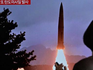 Seorang wanita berjalan melewati televisi yang menayangkan siaran berita dengan file rekaman uji coba rudal Korea Utara, di sebuah stasiun kereta api di Seoul, Korea Selatan, Minggu 19 Maret 2023. (Anthony WALLACE/AFP)