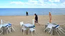 Warga berjalan melewati meja dan kursi kosong di sebuah pantai di Melbourne, Australia, Kamis (19/8/2021). Melbourne melewati 200 hari dalam lockdown keras sejak dimulainya pandemi COVID-19. (William WEST/AFP)