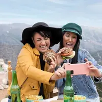 Dua orang perempuan sedang mengambil foto sambil menikmati makanan di atas pegunungan (Foto Dok: Freepik/freepik).