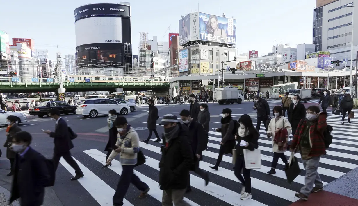 Orang-orang yang mengenakan masker pelindung untuk membantu mengekang penyebaran Virus Corona berjalan di sepanjang penyeberangan pejalan kaki di Tokyo (19/1/2021). Ibukota Jepang itu mengonfirmasi lebih dari 1.200 kasus Virus Corona baru pada 19 Januari 2021. (AP Photo/Eugene Hoshiko)
