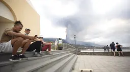 Orang-orang duduk di beberapa anak tangga saat yang lain melihat letusan gunung berapi di dekat El Paso di pulau La Palma di Canaries, Spanyol (20/9/2021). Lava terus mengalir perlahan dari gunung berapi yang meletus di Canary Spanyol Kepulauan di barat laut Afrika. (AP Photo/Gerardo Ojeda)