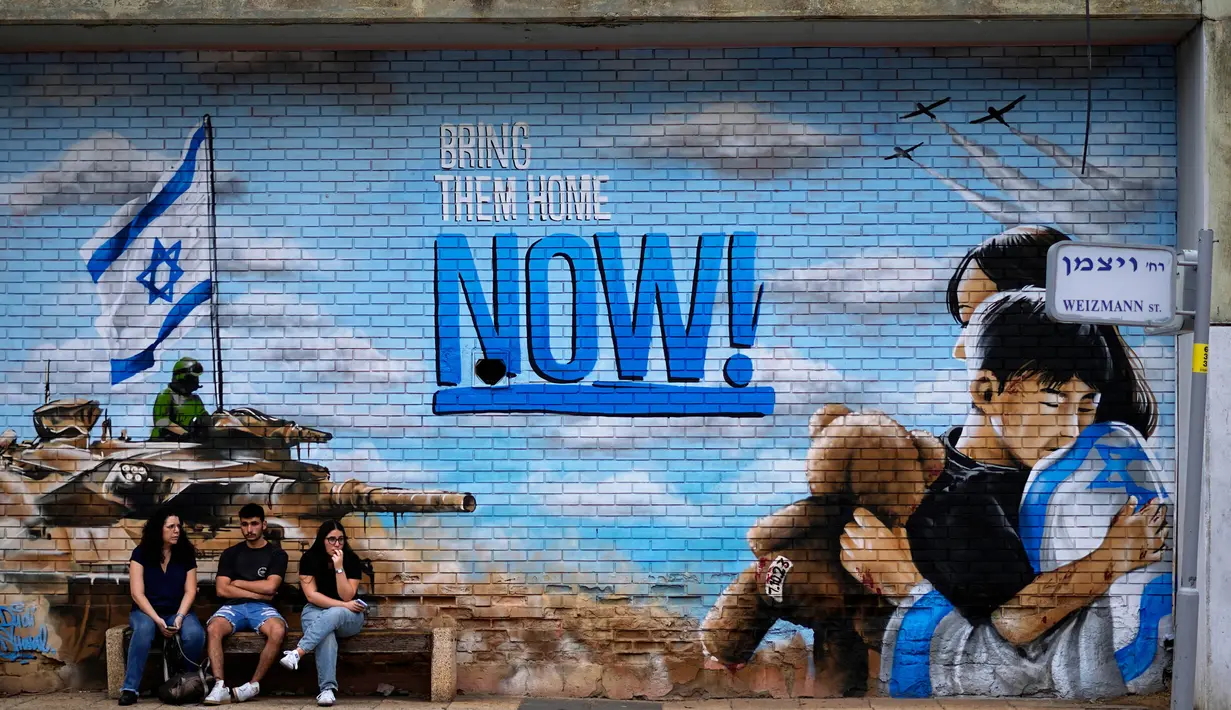 Orang-orang duduk di samping grafiti yang menyerukan kembalinya para sandera yang diculik dalam serangan lintas batas Hamas pada 7 Oktober di Israel, di luar pemakaman di Kfar Saba, Israel, Minggu, 12 November 2023. (AP Photo/Ariel Schalit)