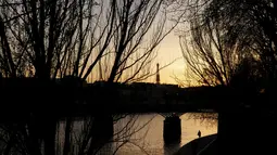 Seorang pria berjalan di tepi sungai Seine dengan Menara Eiffel di latar belakang, saat matahari terbenam, di Paris (29/3/2021). Sungai Seine Namanya berasal dari kata Sequanus dalam bahasa Latin. (AP Photo/Thibault Camus)