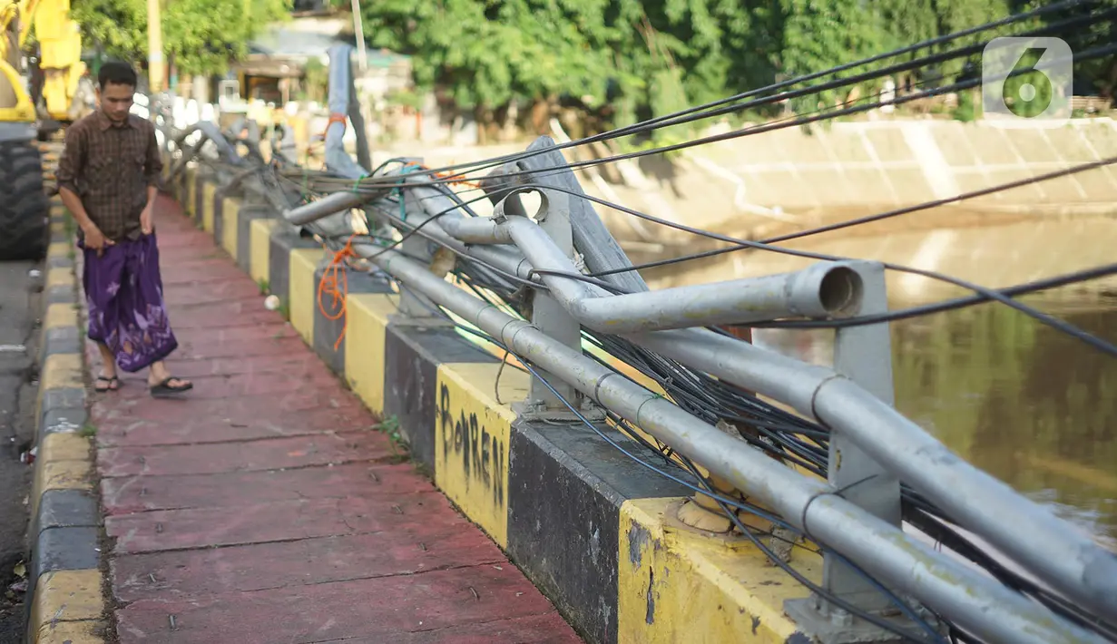 Warga berjalan di samping pagar jembatan yang rusak di kawasan Bukit Duri, Jakarta, Jumat (21/2/2020). Pagar yang rusak akibat penanganan sampah banjir tersebut hingga kini belum juga diperbaiki. (Liputan6.com/Immanuel Antonius)