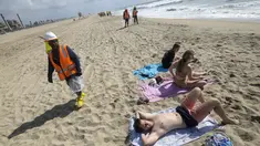 Seorang pekerja berjalan saat pengunjung pantai beristirahat di Huntington Beach, California, Senin (11/10/2021). Pantai Huntington membuka kembali garis pantainya setelah hasil pengujian air kembali dengan jumlah racun terkait minyak yang tidak terdeteksi di air laut. (AP Photo / Ringo HW Chiu)