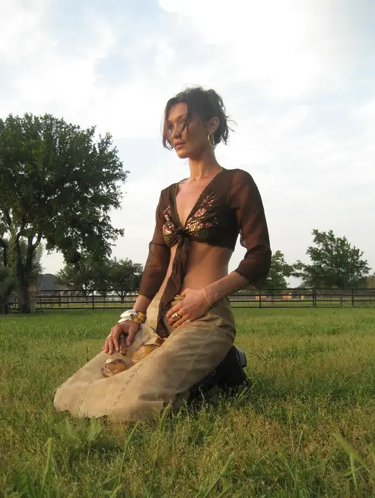 Melihat penampilan manis lainnya dari Bella Hadid. Ia mengenakan cropped top cokelat yang diikat memamerkan otot perutnya yang rata dan rok kulit yang juga bernuansa cokelat muda dan high boots senada. [Foto: Instagram/bellahadid]
