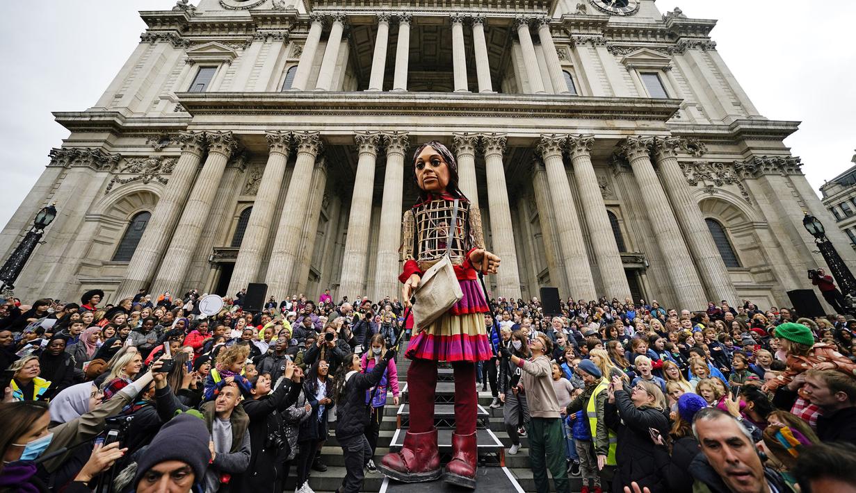 Boneka raksasa Little Amal disambut ratusan warga saat tiba di kota London, Inggris, Sabtu (23/10/2021). Boneka raksasa yang memiliki tinggi 3,5 meter diketahui melakukan perjalanan dengan jarak 8.000 kilometer dari Suriah ke sejumlah negara di Eropa, salah satunya Inggris. (Aaron Chown/PA via AP)