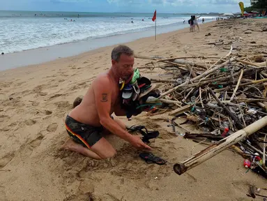 Seorang wisatawan mengumpulkan sampah yang berserakan di Pantai Kuta, Badung, Bali, Kamis (20/4/2023). (merdeka.com/Arie Basuki)
