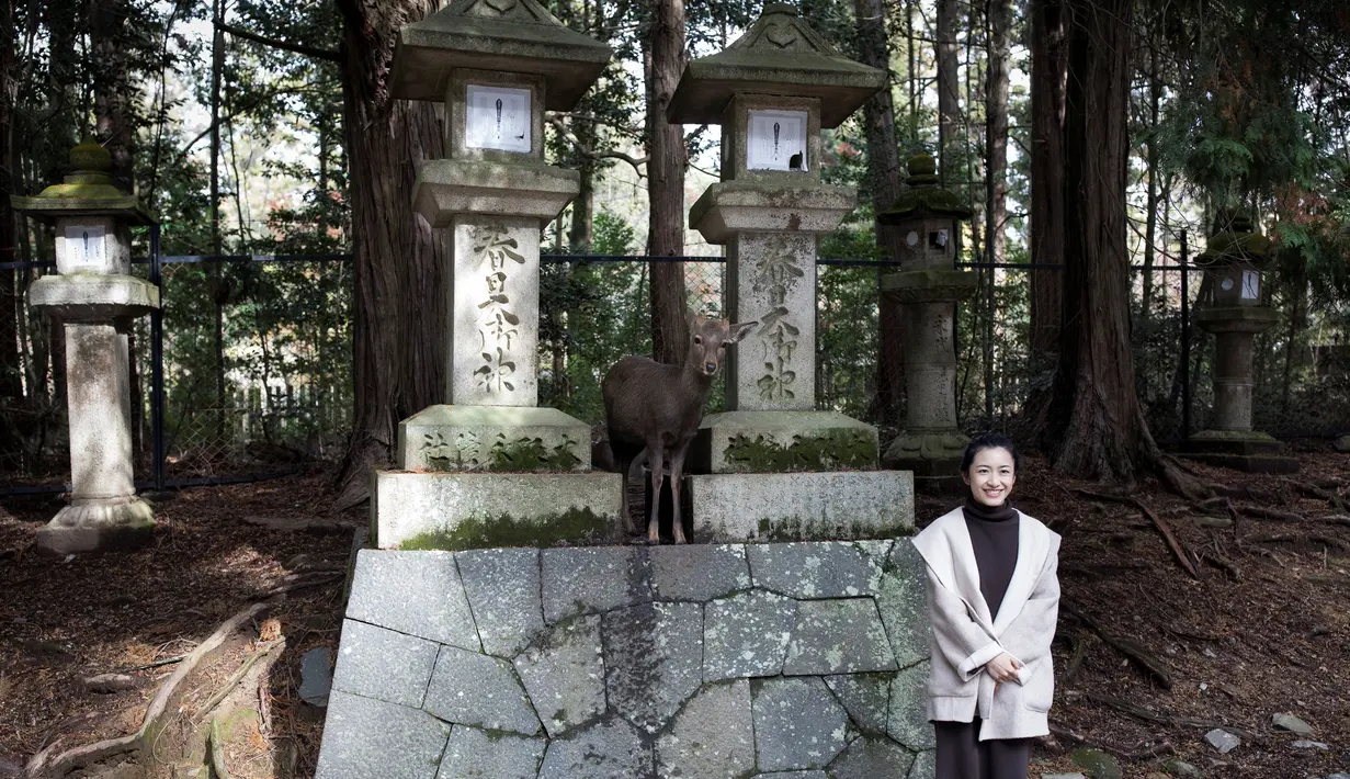 Seorang turis berfoto dengan rusa di taman Nara, kota Nara, Jepang pada 7 Desember 2018. Begitu memasuki kawasan ini, para pengunjung akan disambut dengan banyak rusa yang berkeliaran bebas. (Behrouz MEHRI / AFP)