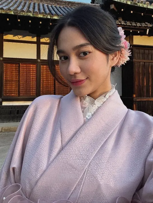 Wajahnya dipulas makeup nuansa pink dari blush on dan lipstiknya. Rambutnya disanggul modern dengan hiasan bunga pinknya. [@azizahsalsha_]
