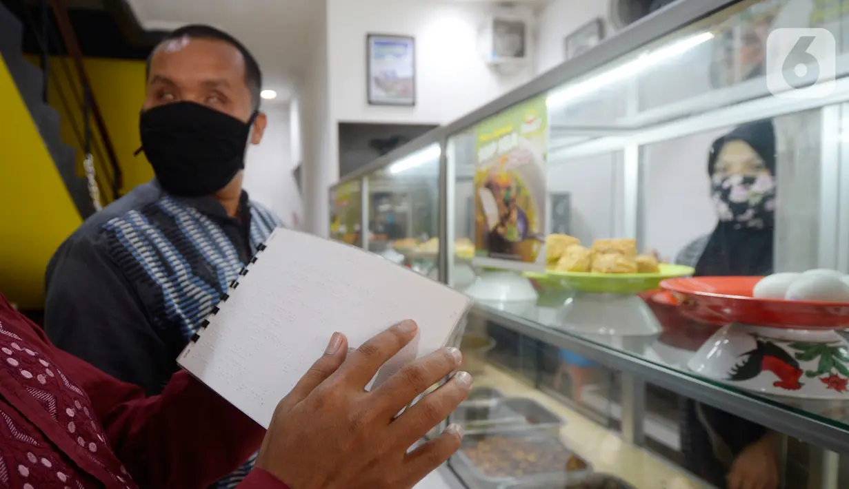 Pengunjung tuna netra memilih menu makanan menggunakan panduan buku braille di Warteg FAST, Graha Raya Bintaro, Tangerang Selatan, Banten, Kamis (3/12/2020). Hari ini diperingati Hari Penyandang Disabilitas Internasional. (merdeka.com/Dwi Narwoko)