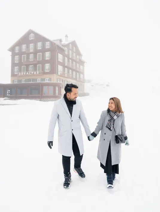 Kali ini keduanya berpose di tengah salju. Dengan outfit bernuansa abu-abu, Kiky memilih long coat berwarna abu-abu gelap dipadu pleated skirt hitam. Sedangkan suaminya memilih mengenakan dalaman berwarna hitam, ditumpuk long coat abu-abu yang lebih cerah, dipadu celana panjang hitam. Keduanya melilitkan syal di leher masing-masing. Foto: Instagram.