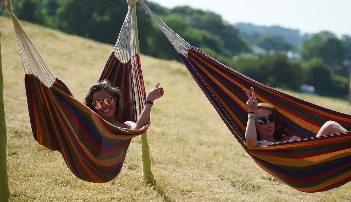 Dua wanita bersantai di tempat tidur gantung saat menghadiri Festival Musik Glastonbury di Worthy Farm, di Somerset, Inggris, (22/6). Festival Glastonbury merupakan festival musik paling populer di dunia. (AFP Photo/Oli Scarff)