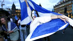 Seorang fans wanita menari sambil mengibarkan bendera Skotlandia saat merayakan hasil imbang melawan Inggris di Glasgow, Skotlandia, Jumat (18/6/2021). (Robert Perry/PA via AP)
