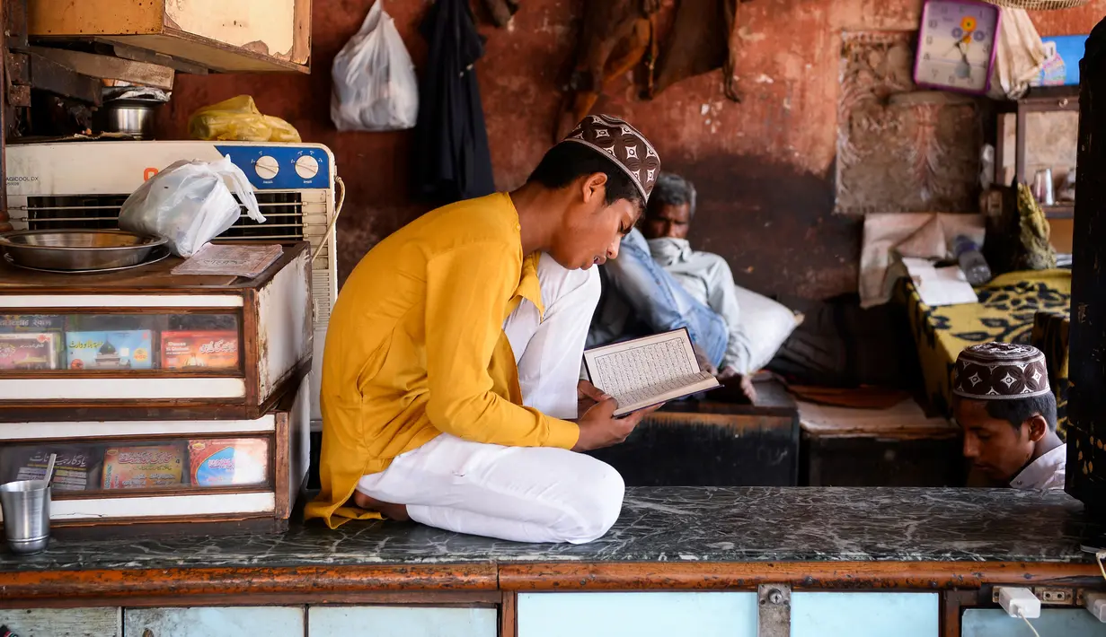 Seorang anak membaca Alquran di sebuah toko yang tutup selama bulan Ramadan saat penerapan lockdown di New Delhi, Senin (4/5/2020). Di emperan toko-toko yang tutup, umat muslim melaksanakan salat jemaah dengan menjaga jarak aman dan beberapa lainnya membaca kitab suci Alquran. (Sajjad HUSSAIN/AFP)