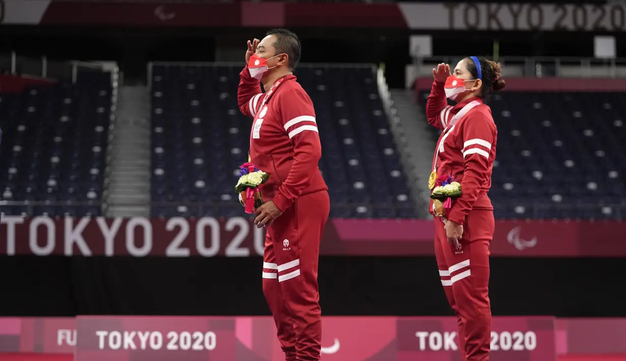 Hary Susanto dan Leani Ratri Oktila memberi hormat kepada bendera sambil menyanyikan lagu kebangsaan setelah menerima medali emas pada ganda campuran cabang badminton nomor SL3-SU5 Paralimpiade Tokyo 2020, Minggu (5/9/2021). Indonesia menambah medali emas lewat Hary/Leani. (AP/Kiichiro Sato)