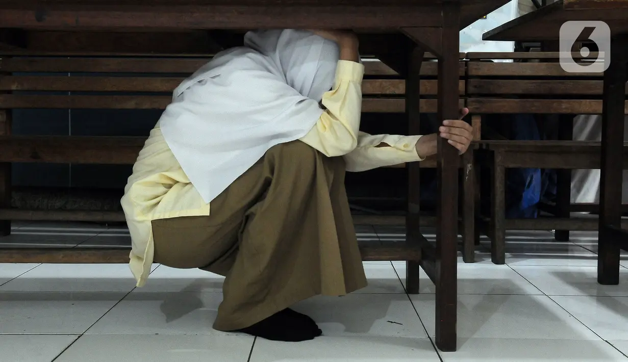 Seorang santriwati berlindung di bawah meja saat pelatihan tanggap bencana dan kebakaran yang dilakukan oleh Badan Penanggulangan Bencana Daerah (BPBD) DKI Jakarta bersama Pemadam Kebakaran DKI Jakarta di Madrasah Aliyah Swasta Persatuan Islam (MAS Persis) 69, Matraman, Jakarta, Selasa (19/9/2023). (merdeka.com/Imam Buhori)