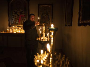 Seorang pria menyalakan lilin saat kebaktian Minggu di sebuah gereja Ortodoks di Bucha, di pinggiran Kiev, Ukraina, Minggu, 10 April 2022. Invasi Rusia ke Ukraina hingga saat ini telah berlangsung selama 46 hari. (AP Photo/Rodrigo Abd)