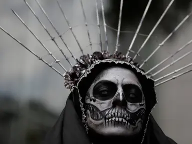 Seorang wanita mengenakan kostum tengkorak menunggu dimulainya Prosesi Grand Catrinas, untuk menandai perayaan Day of The Dead, di Mexico City, Minggu (22/10). Dalam prosesi tersebut warga berdandan menyerupai kerangka. (AP/Rebecca Blackwell)